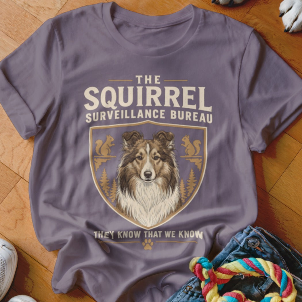 A dusty purple t-shirt displays text and a crest featuring a Shetland Sheepdog and squirrels.