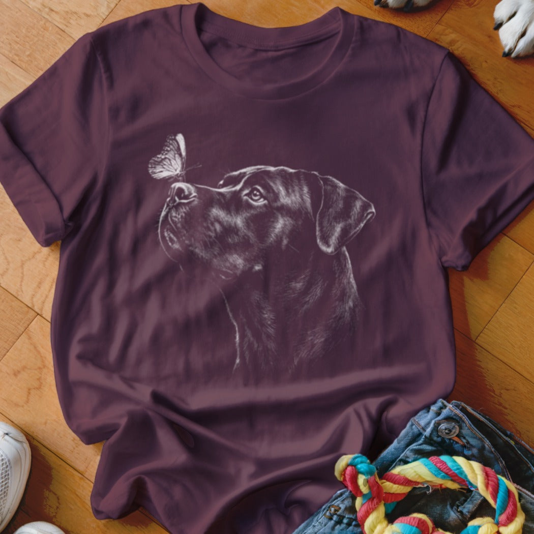 A maroon short-sleeve t-shirt with a white line drawing of a dog looking at a butterfly on its nose.