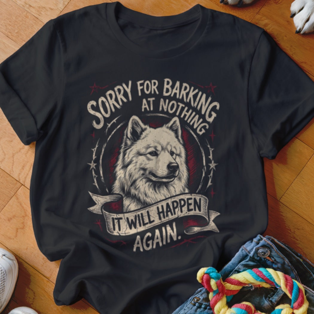 A black t-shirt features a graphic of a white dog, text reading "SORRY FOR BARKING AT NOTHING IT WILL HAPPEN AGAIN," and a red circular emblem on a wooden floor.