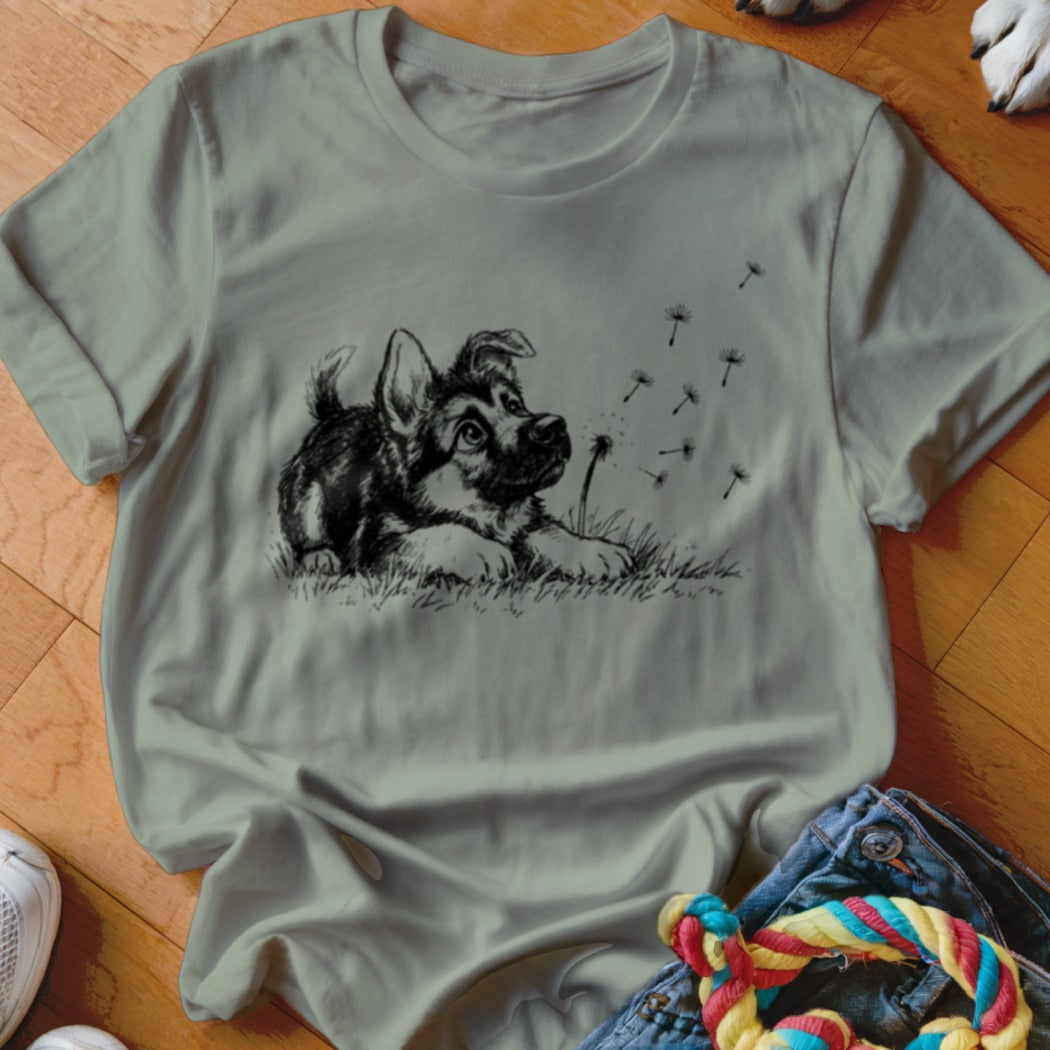 Sage green crewneck t-shirt featuring a black graphic of a puppy watching floating dandelion seeds.