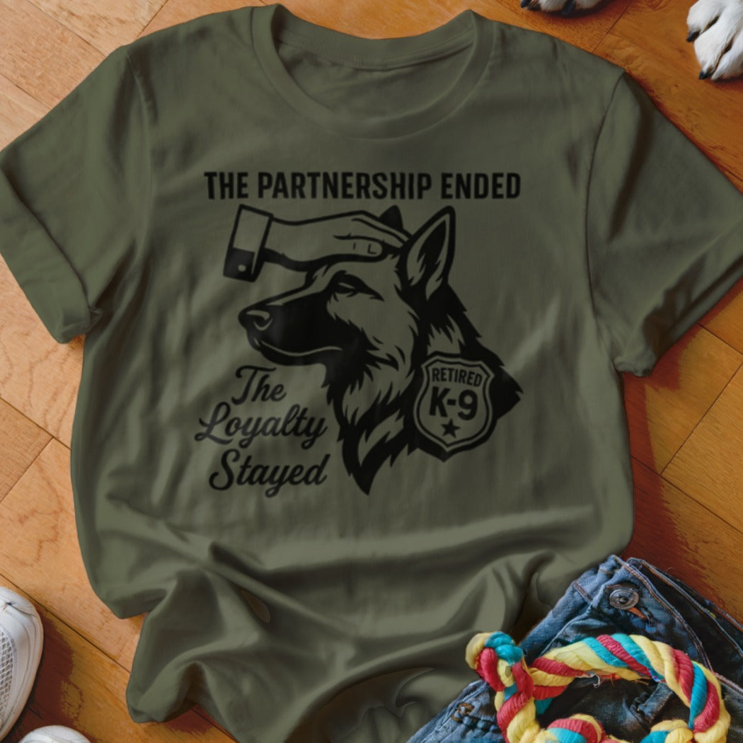 Olive green t-shirt with black graphic: German Shepherd head, hand, text "The partnership ended", "The Loyalty Stayed", and "Retired K-9".