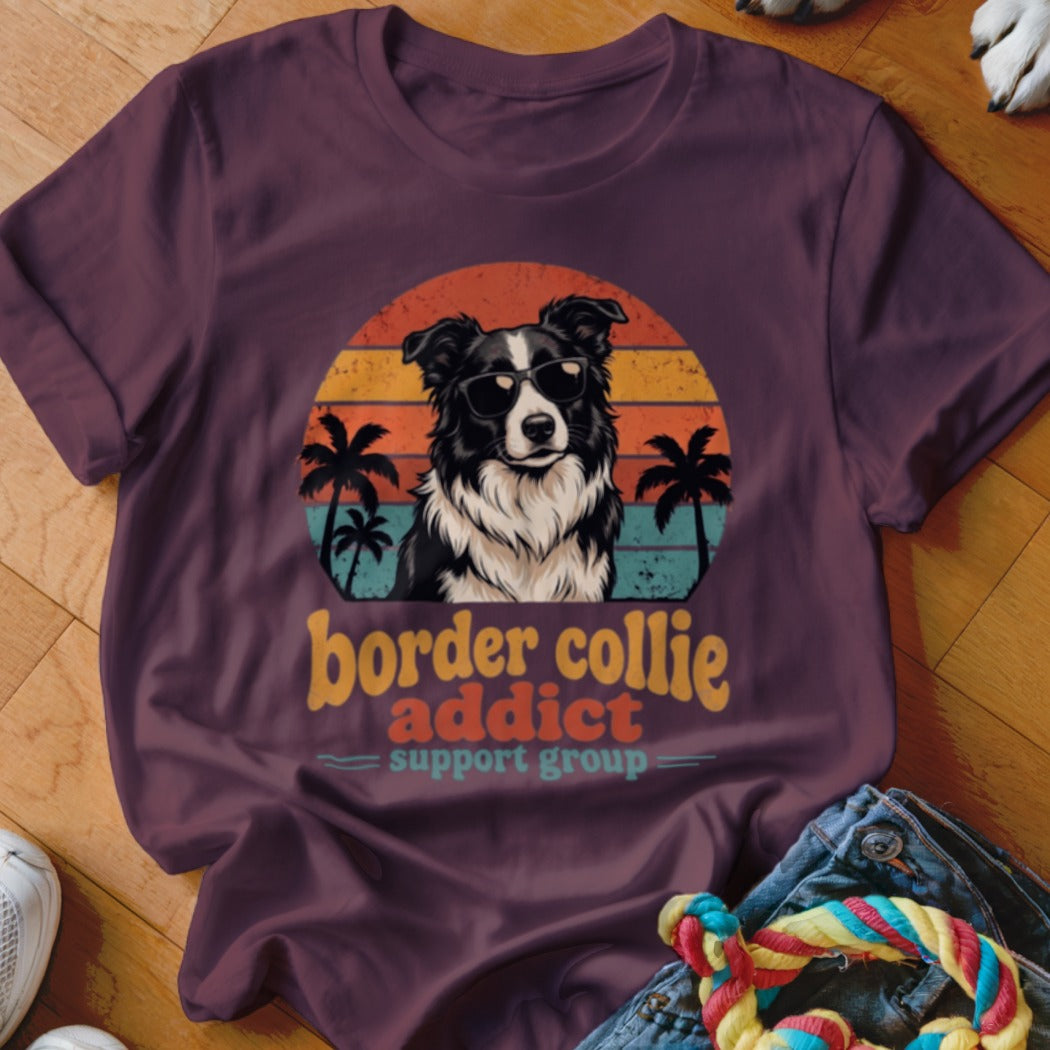 A purple crewneck t-shirt featuring a retro graphic of a Border Collie wearing sunglasses, framed by a sunset, palm trees, and text reading Border Collie Addict Support Group.