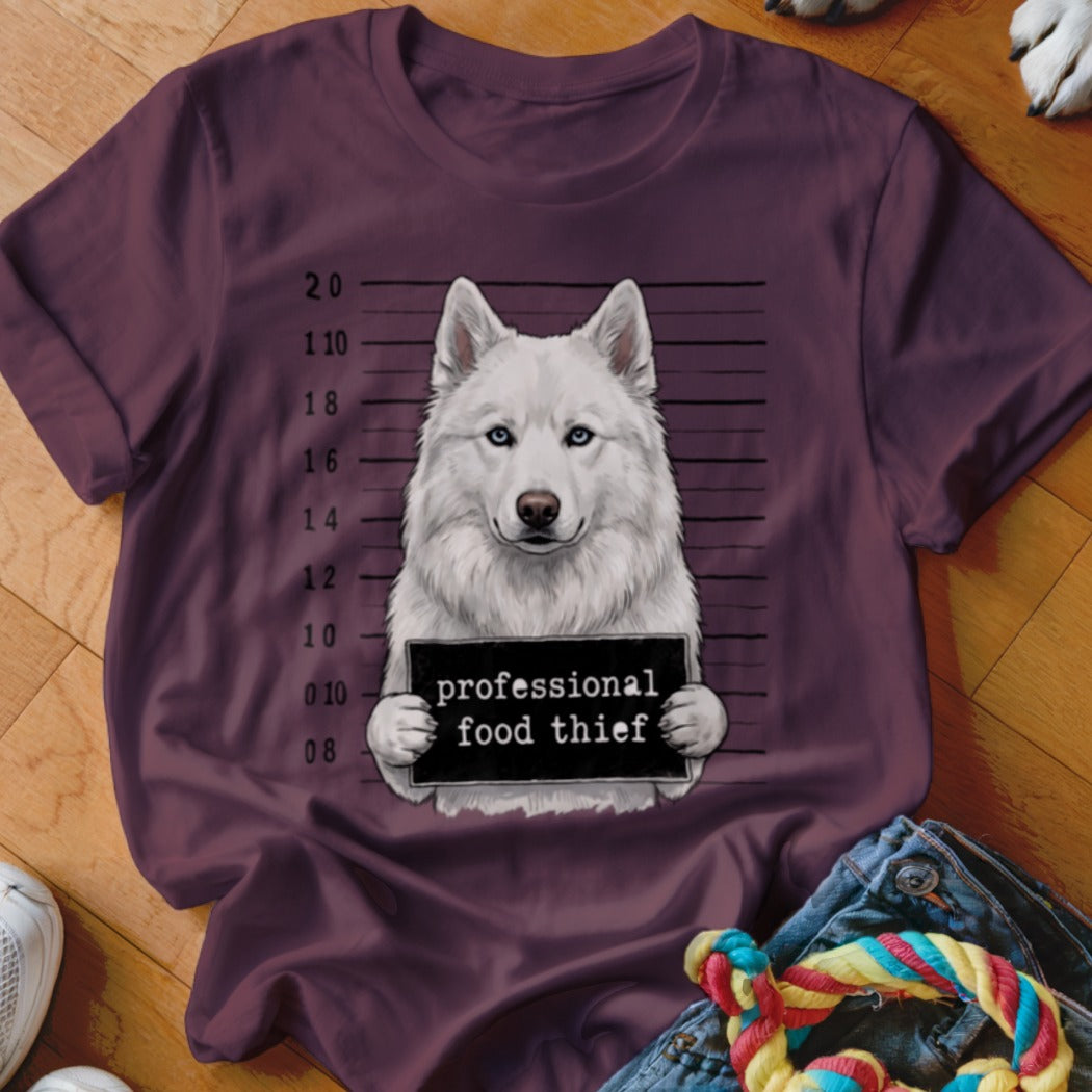 White husky mugshot on a maroon t-shirt, holding a sign reading "professional food thief".