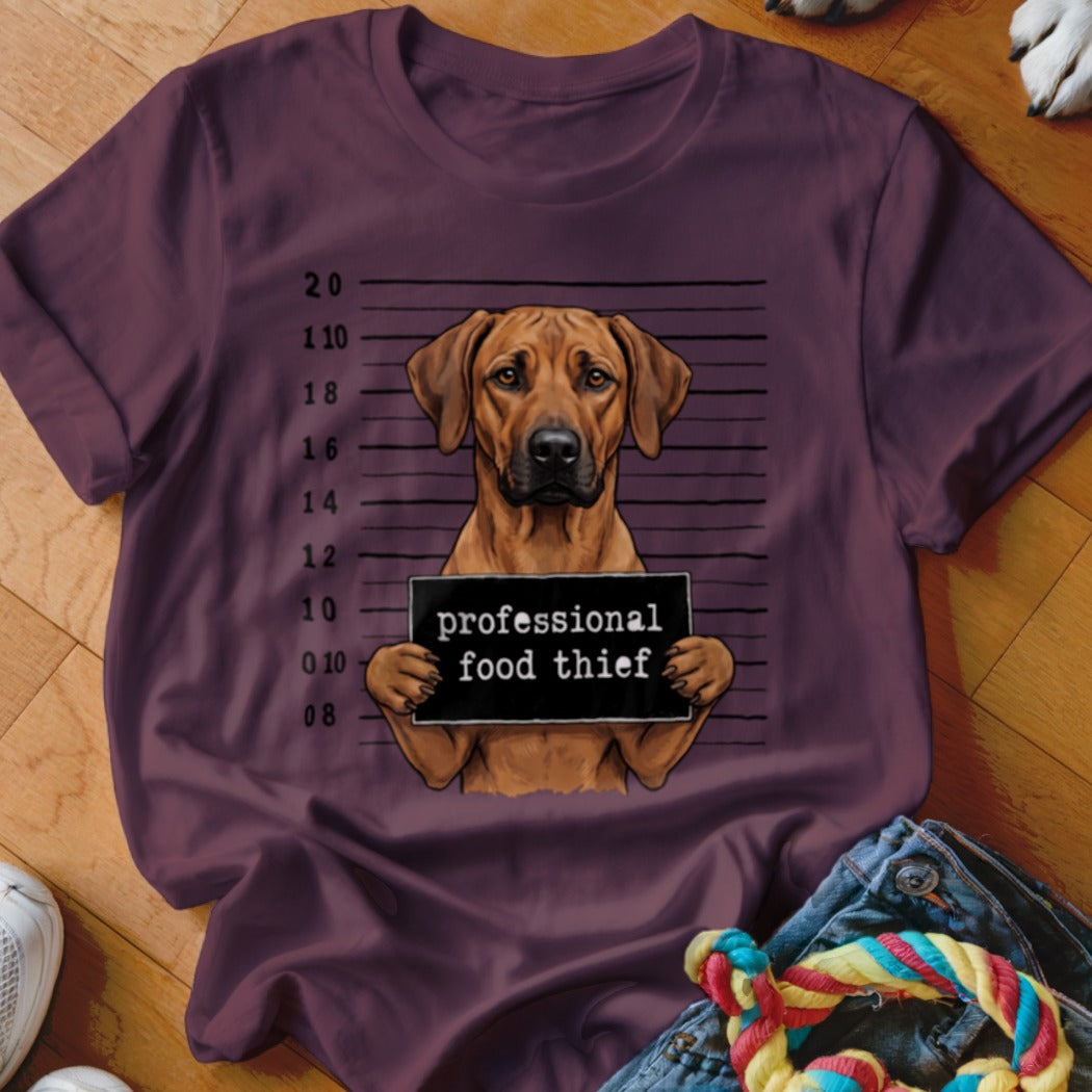 Brown dog mugshot with "professional food thief" sign on burgundy t-shirt.