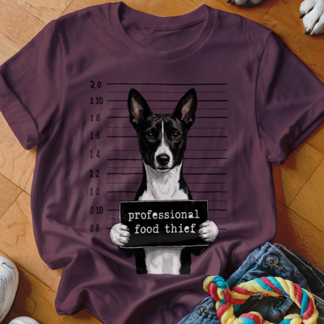 Basenji dog mugshot with "professional food thief" sign on t-shirt.