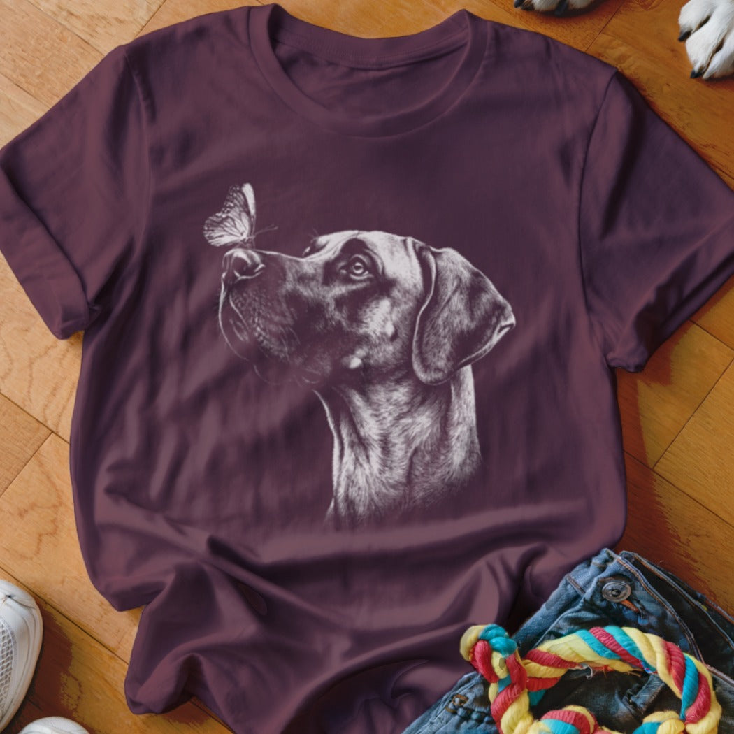 A dark purple t-shirt featuring a white sketch graphic of a dog looking at a butterfly on its nose.