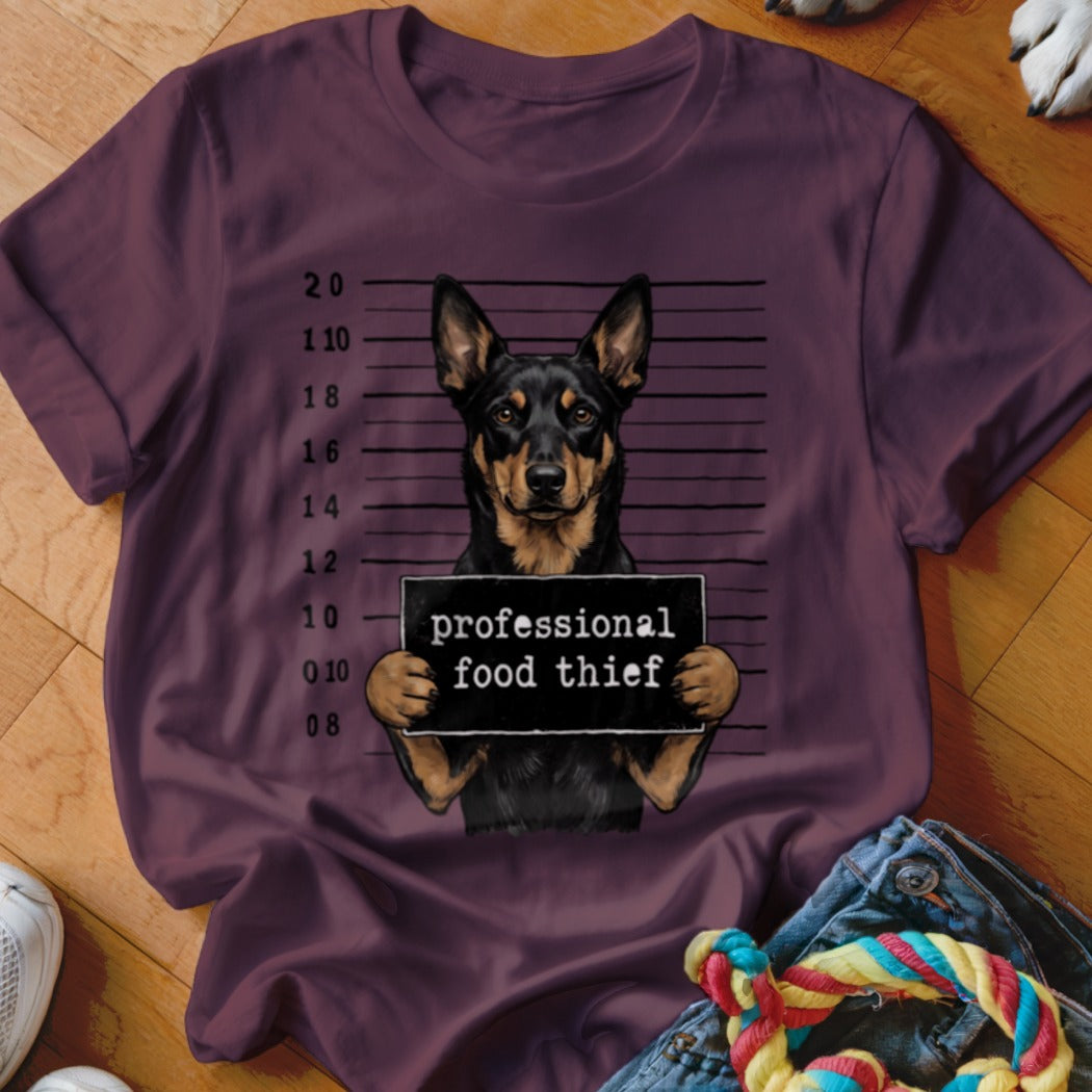 Dog mugshot with "professional food thief" sign on maroon t-shirt.
