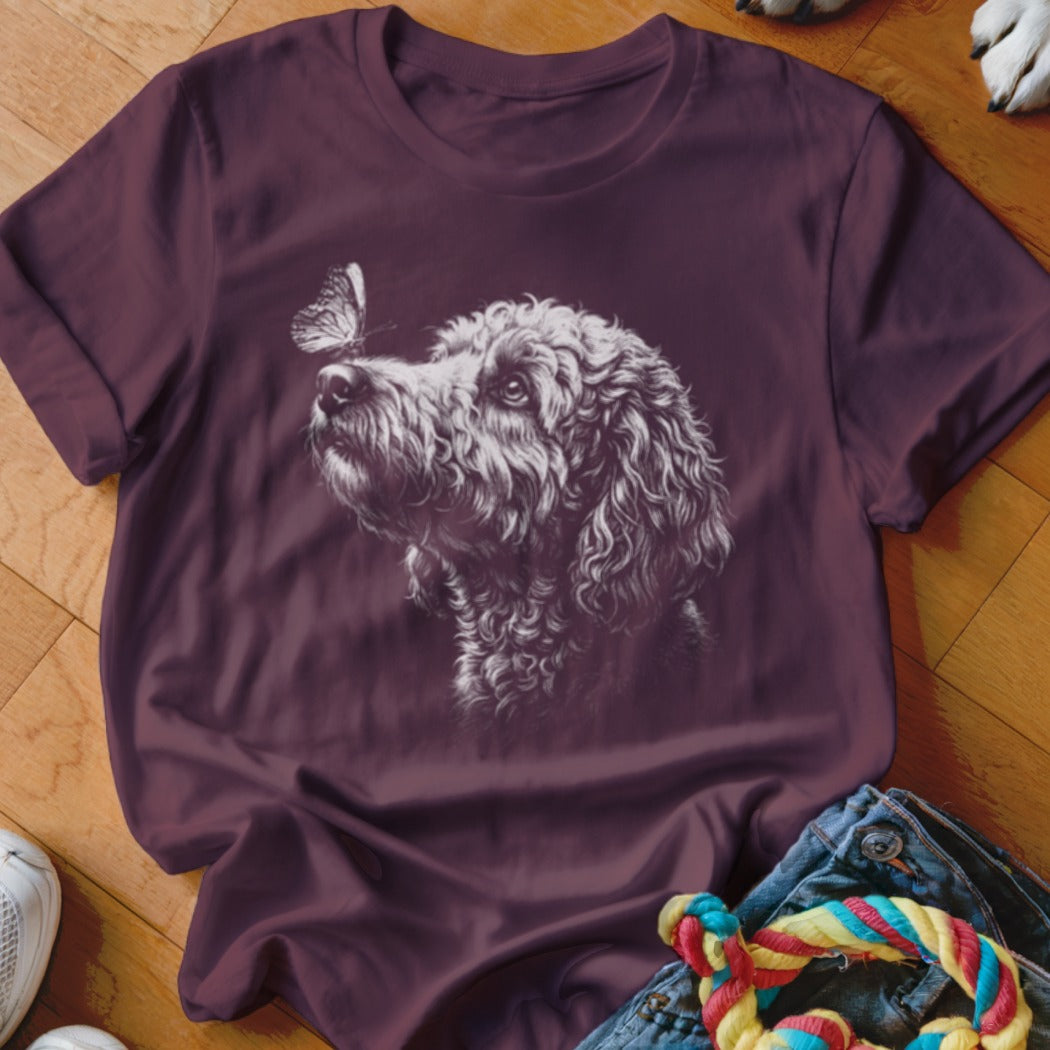 A dark purple short-sleeved t-shirt featuring a white sketch of a curly dog looking at a butterfly.
