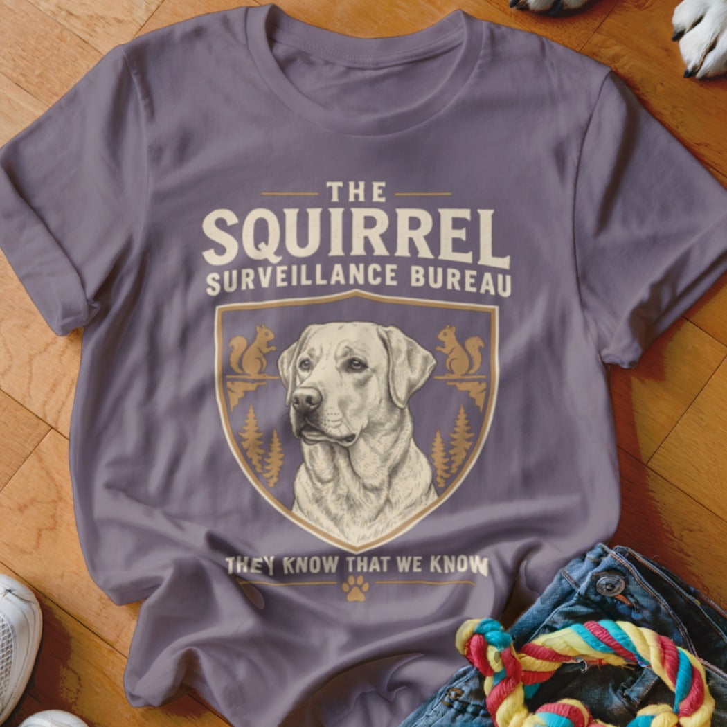 A purple t-shirt featuring a Labrador and text reading The Squirrel Surveillance Bureau.