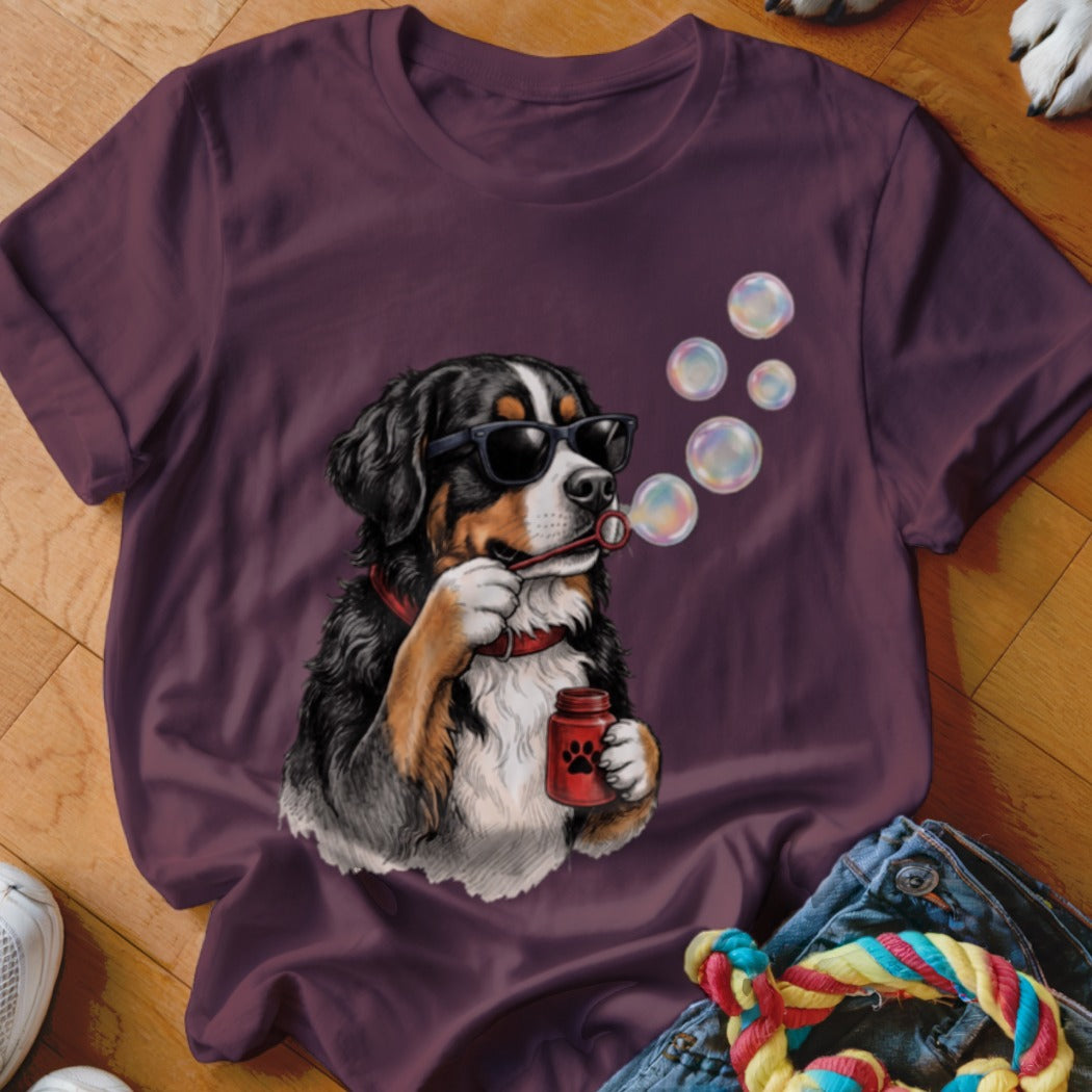 A dark purple t-shirt featuring a graphic of a Bernese Mountain Dog wearing sunglasses and blowing bubbles.