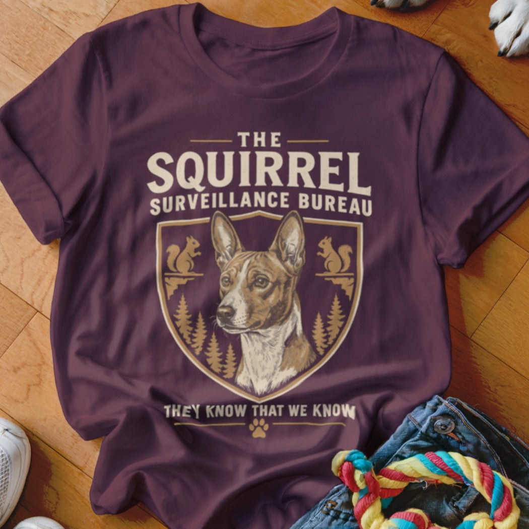 Maroon t-shirt featuring a dog graphic, text reading The Squirrel Surveillance Bureau, and pine tree illustrations.