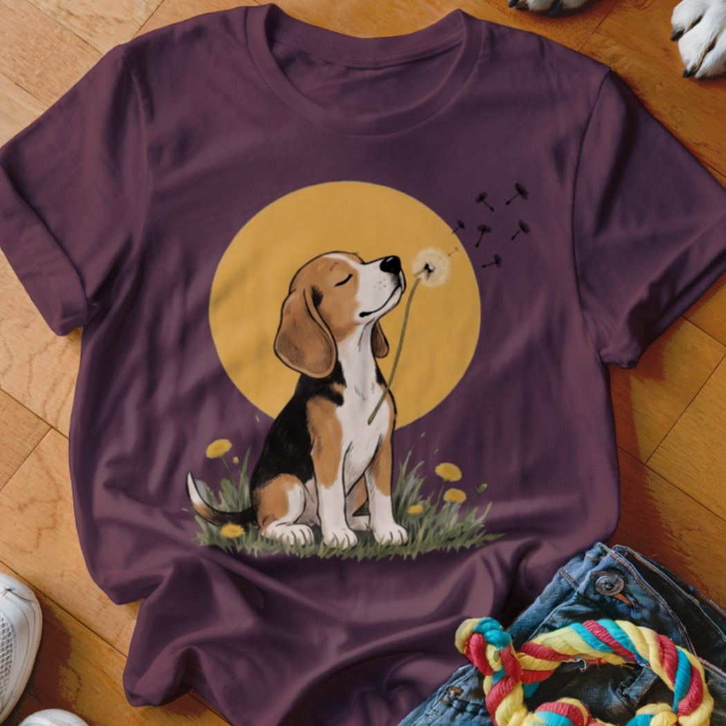 A dark purple t-shirt featuring a graphic of a beagle blowing dandelion seeds against a yellow sun.