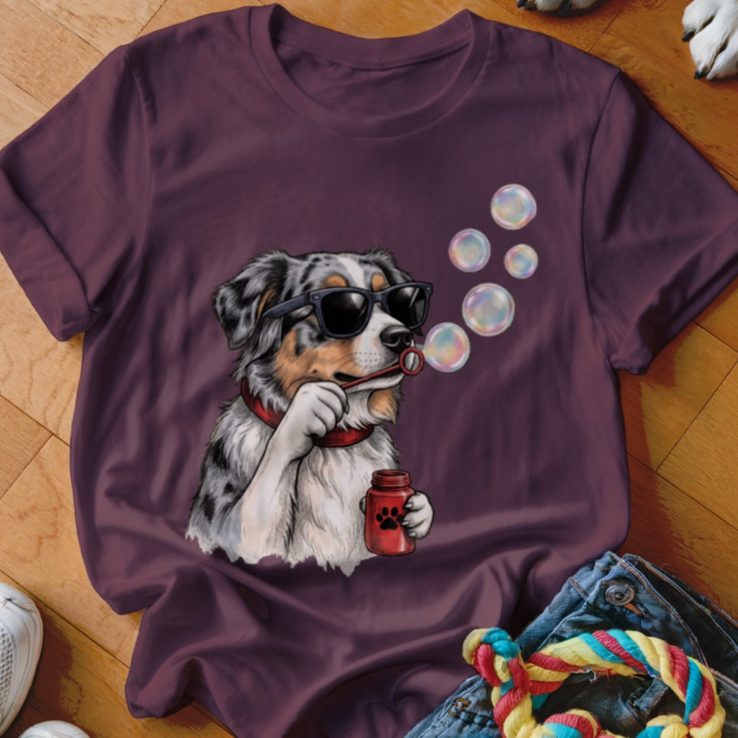 Plum-colored t-shirt featuring a graphic of an Australian Shepherd wearing sunglasses and blowing bubbles.