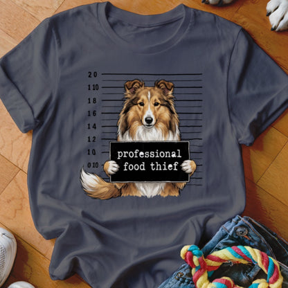 Shetland sheepdog mugshot with "professional food thief" sign on t-shirt.