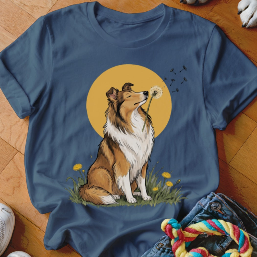 Blue t-shirt featuring an illustration of a Shetland Sheepdog blowing a dandelion against a yellow circle background.