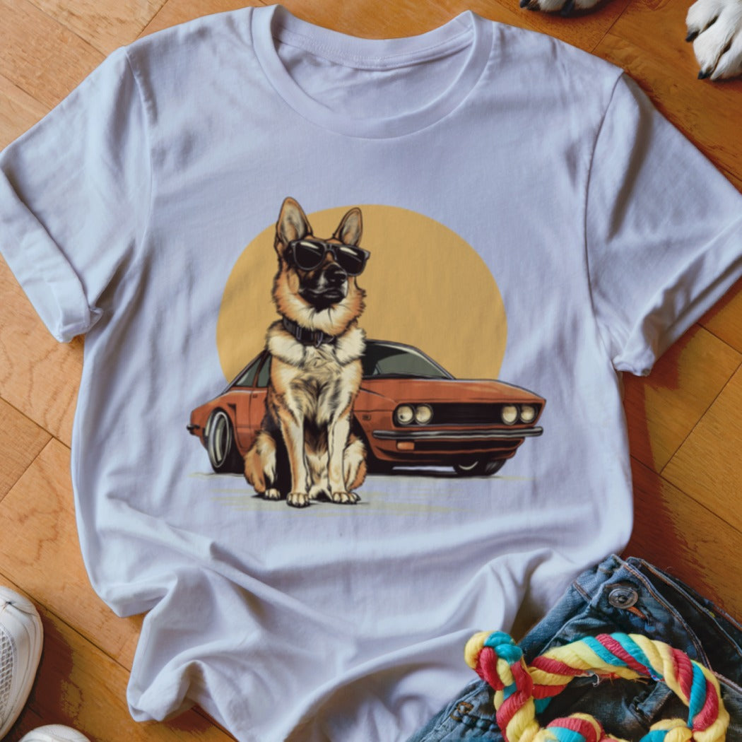 German Shepherd wearing sunglasses sits in front of a vintage car and sun on a white t-shirt.