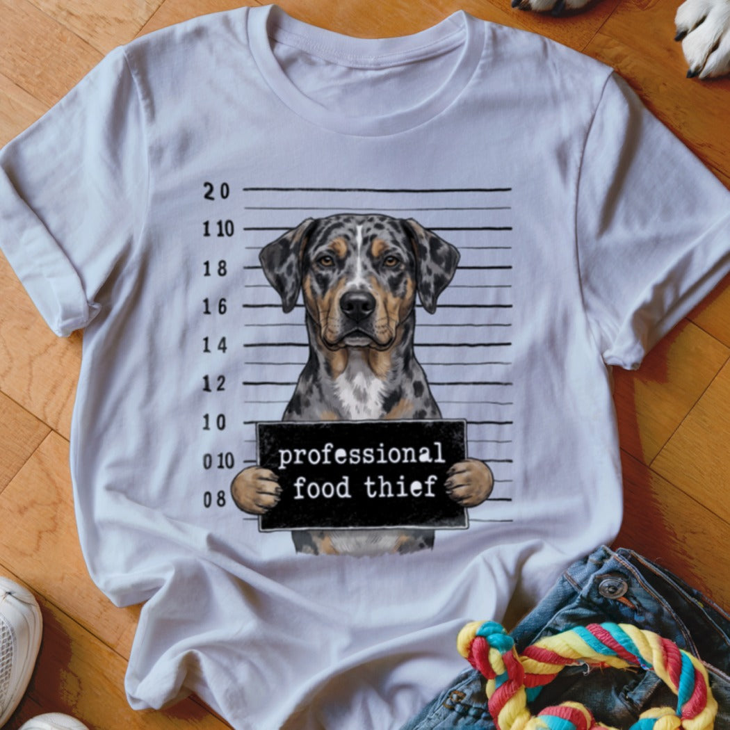 Dog with "professional food thief" sign in mugshot background on white t-shirt.