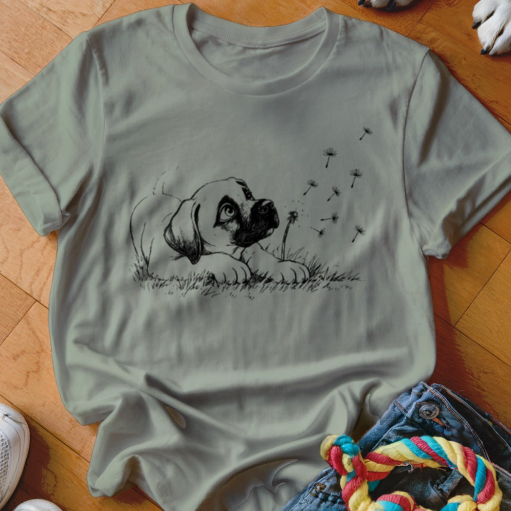 Sage green crewneck t-shirt featuring a black line drawing of a puppy watching floating dandelion seeds.