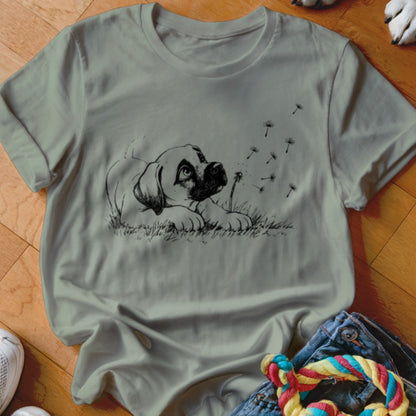 Sage green crewneck t-shirt featuring a black line drawing of a puppy watching floating dandelion seeds.