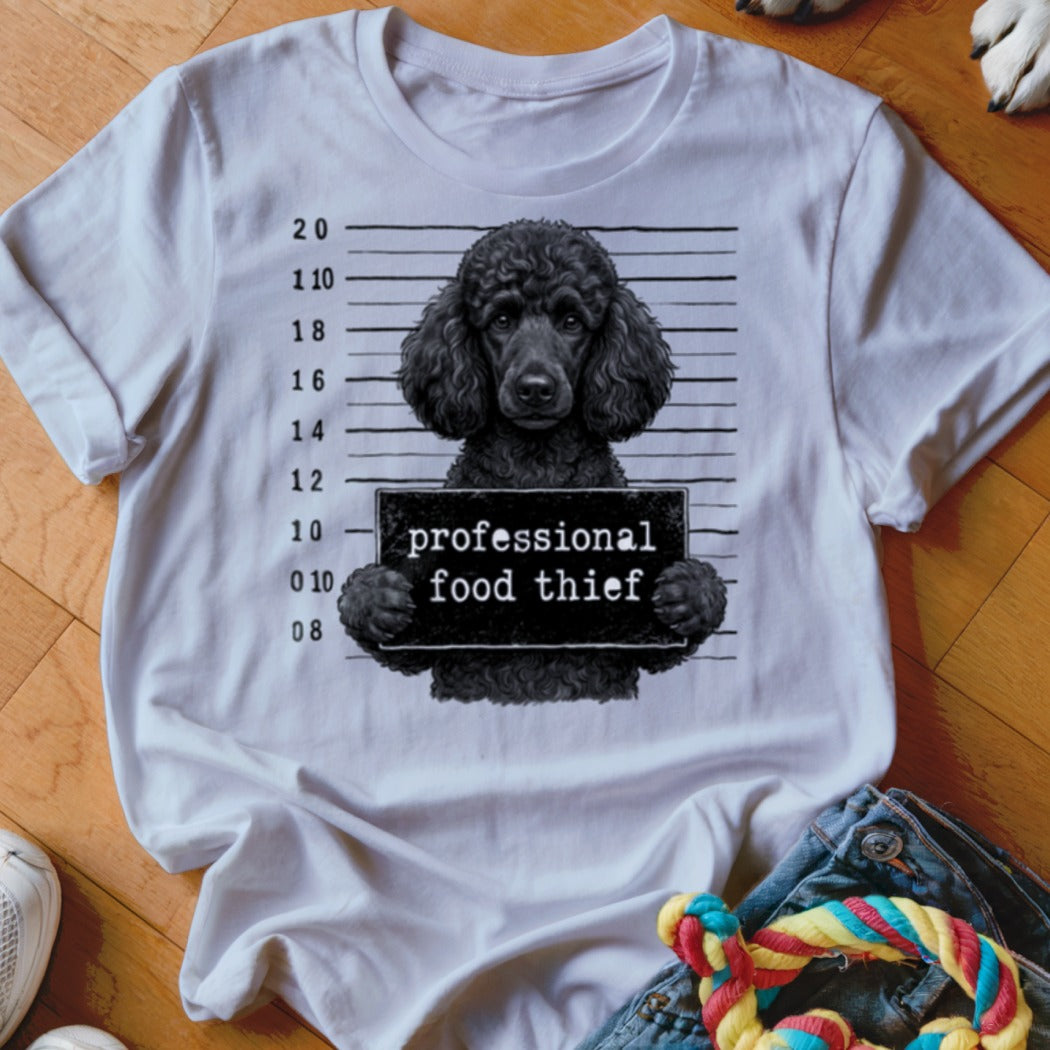 Black poodle mugshot with "professional food thief" sign on white t-shirt.