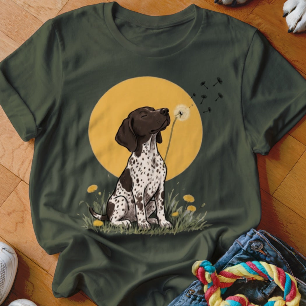 A dark green t-shirt features a graphic of a spotted puppy blowing dandelion seeds against a yellow circle background.