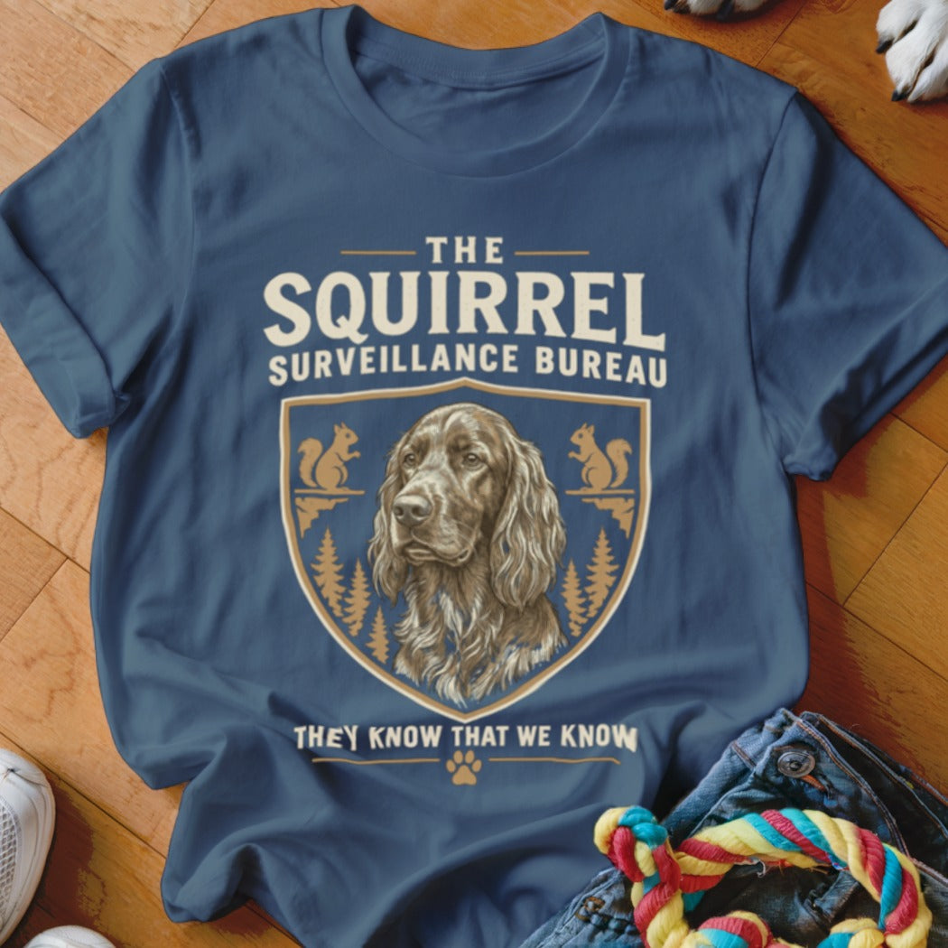 Blue crewneck t-shirt featuring a crest with a spaniel, pine trees, squirrels, and the text The Squirrel Surveillance Bureau.