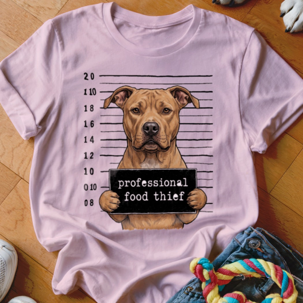 Pit bull mugshot with sign reading "professional food thief" on pink t-shirt.