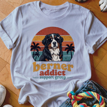 A white t-shirt featuring a retro graphic of a Bernese Mountain Dog wearing sunglasses against a sunset.