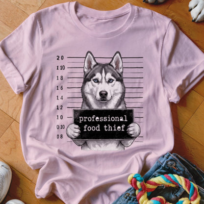 Husky mugshot on pink t-shirt, holding "professional food thief" sign.