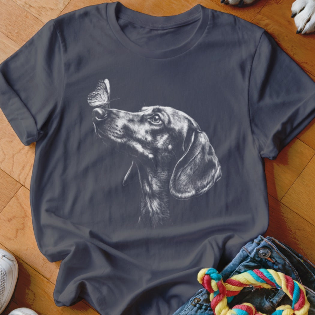 Dark gray t-shirt featuring a white sketch graphic of a dachshund looking at a butterfly.