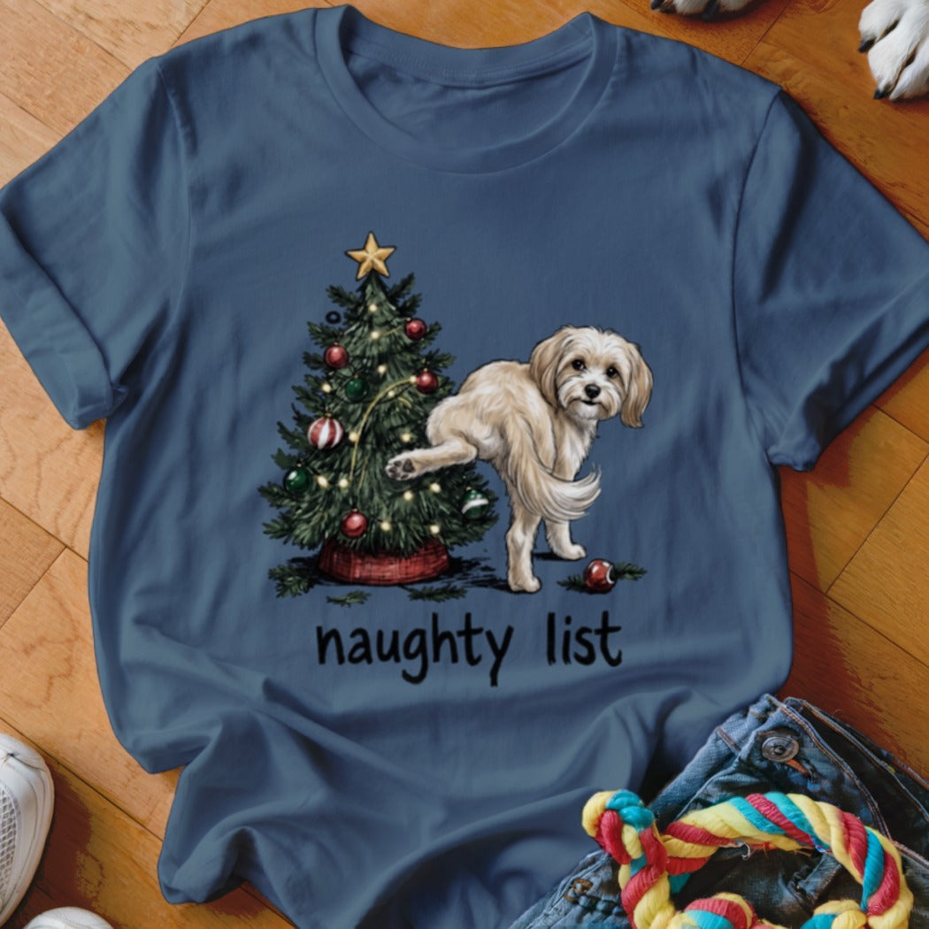Dog near Christmas tree with text "naughty list" on blue shirt.