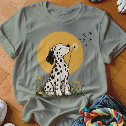 Sage green t-shirt featuring a graphic of a Dalmatian puppy blowing dandelion seeds against a yellow sun.