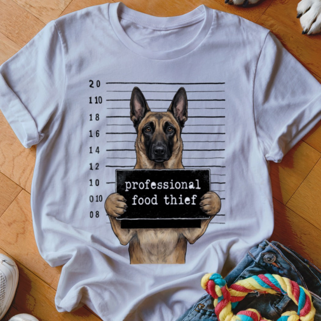 German Shepherd mugshot with "professional food thief" sign on a t-shirt.