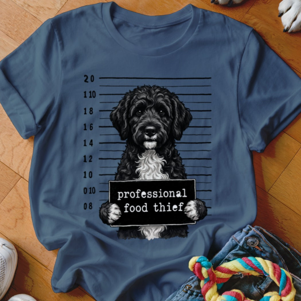 Black poodle with white chest holding "professional food thief" sign on mugshot background.