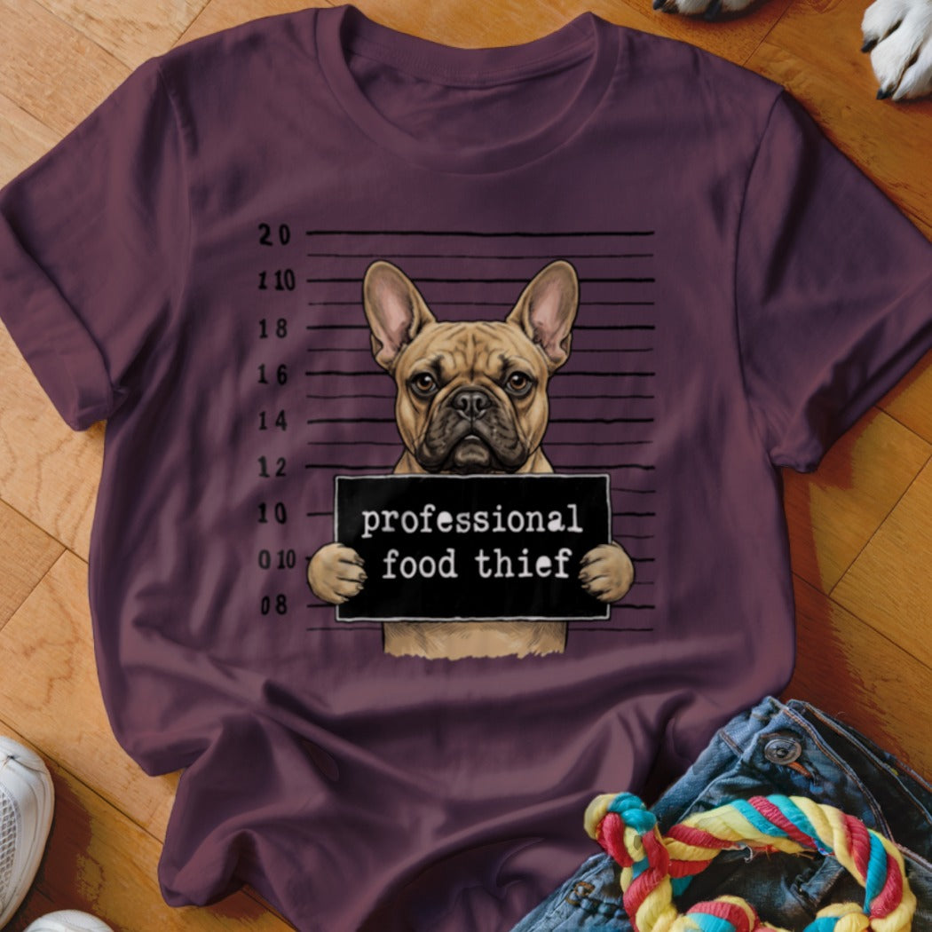 French bulldog mugshot with "professional food thief" sign on plum t-shirt.