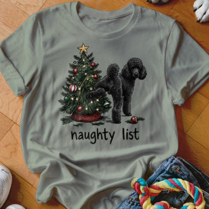 Black poodle standing next to a decorated Christmas tree with "naughty list" text.