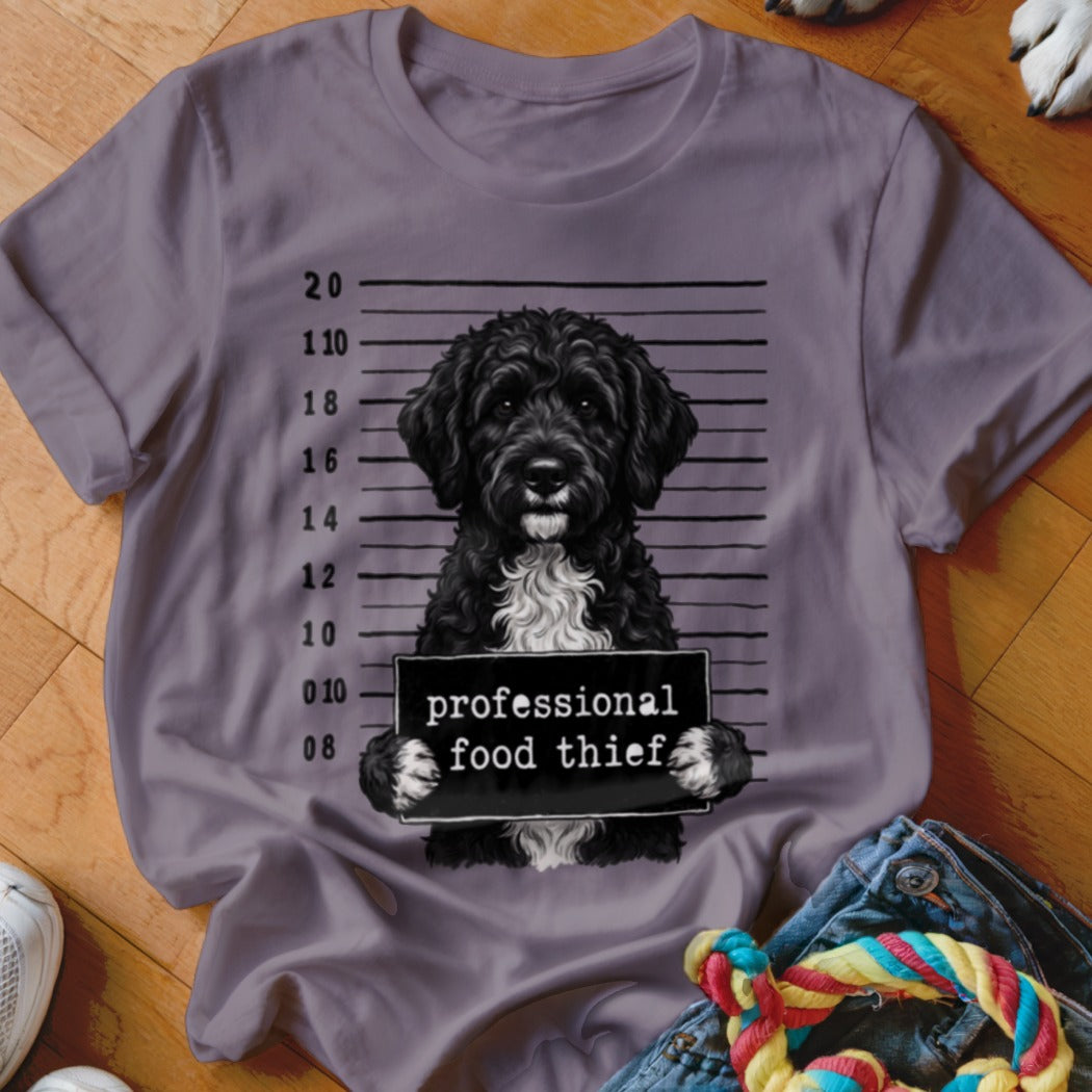 Black dog with white chest holding a "professional food thief" sign in a mugshot.