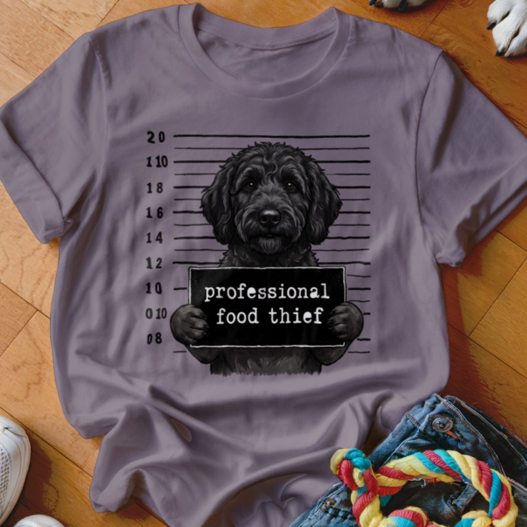 Black dog mugshot with "professional food thief" sign on a grey t-shirt.