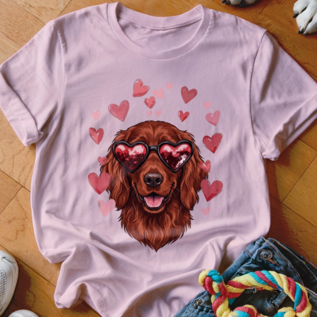 A light pink t-shirt featuring an illustration of a brown dog wearing heart-shaped sunglasses surrounded by pink hearts.