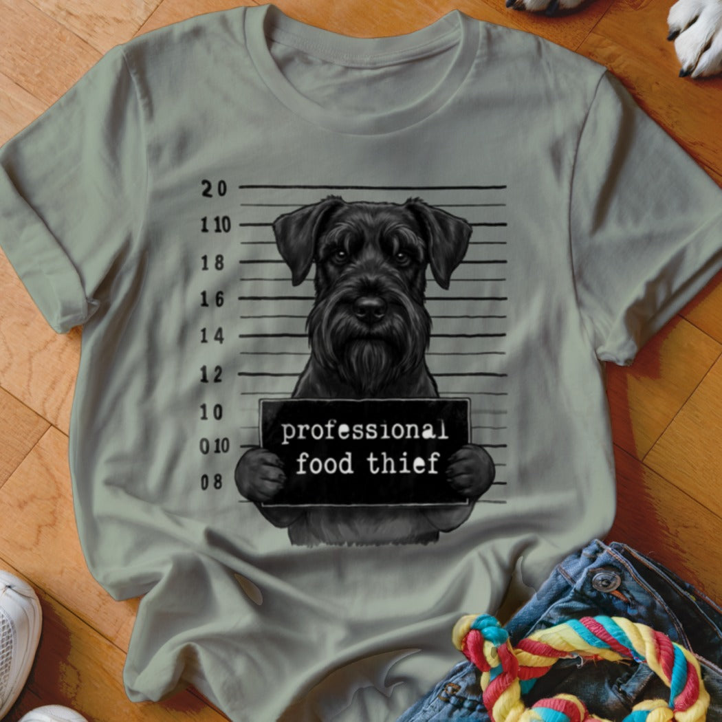Black schnauzer mugshot with "professional food thief" sign on t-shirt.