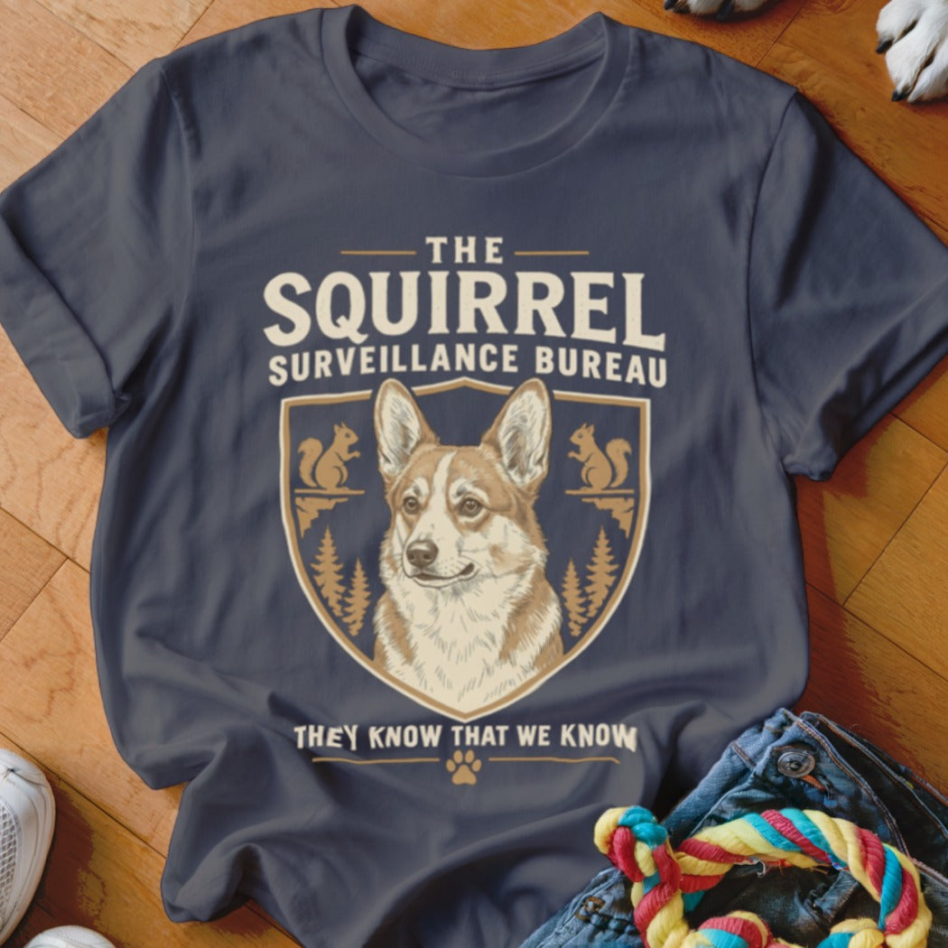 A dark gray t-shirt with a graphic of a corgi, squirrels, and the text The Squirrel Surveillance Bureau.