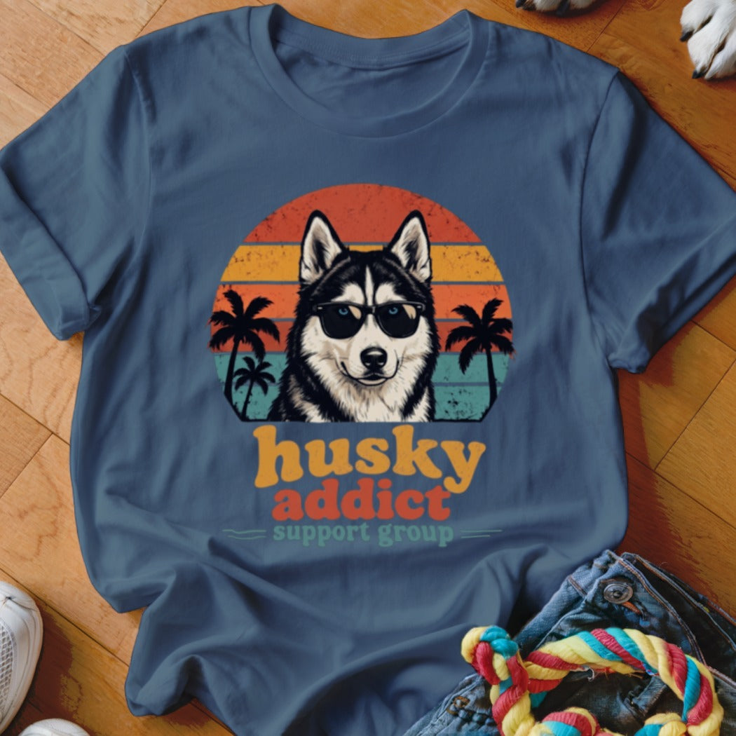 A blue t-shirt featuring a graphic of a husky wearing sunglasses against a retro sunset.