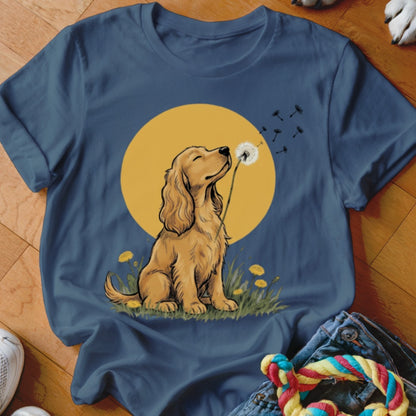 A blue t-shirt featuring an illustration of a golden cocker spaniel blowing a dandelion.