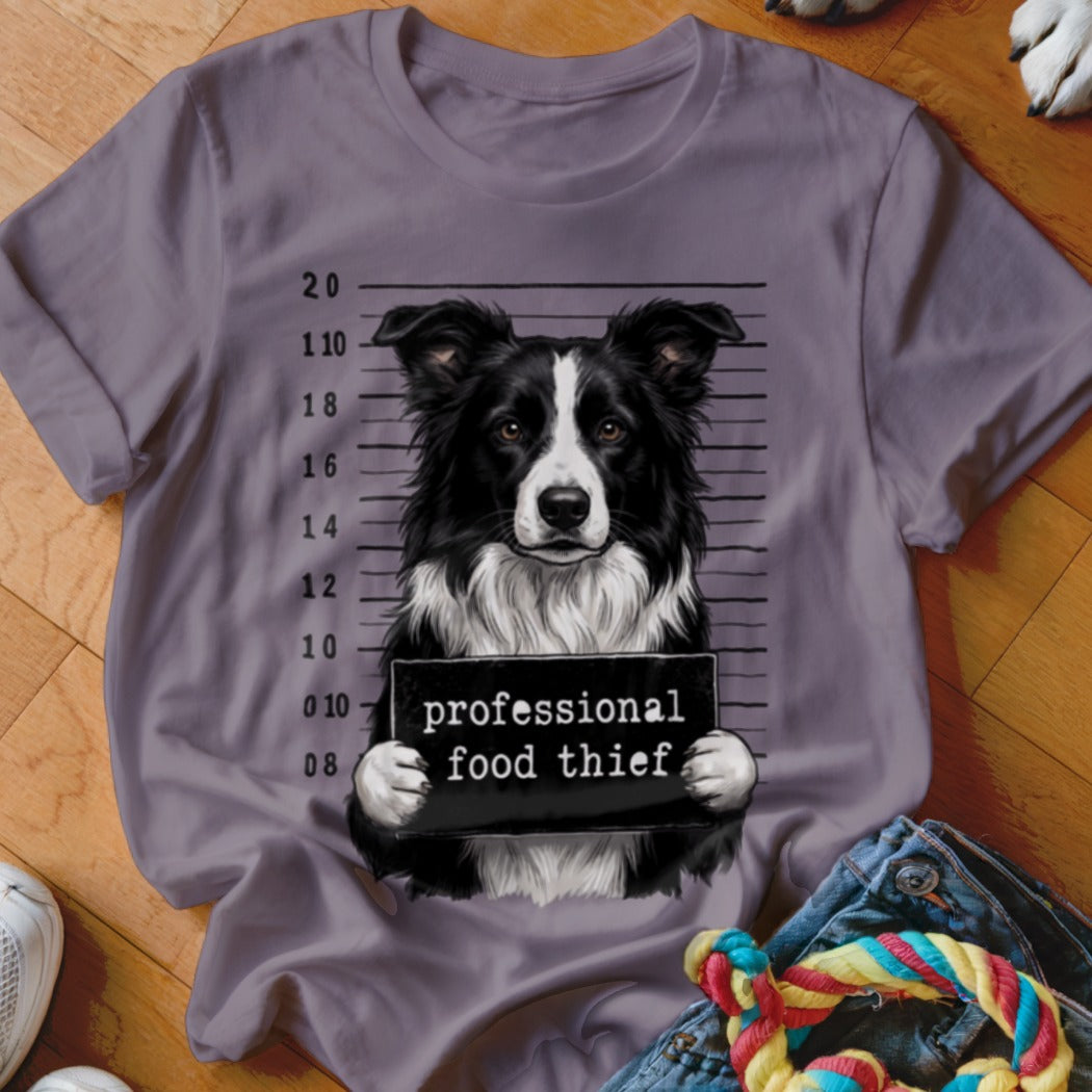 Border collie mugshot with "professional food thief" sign on a t-shirt.