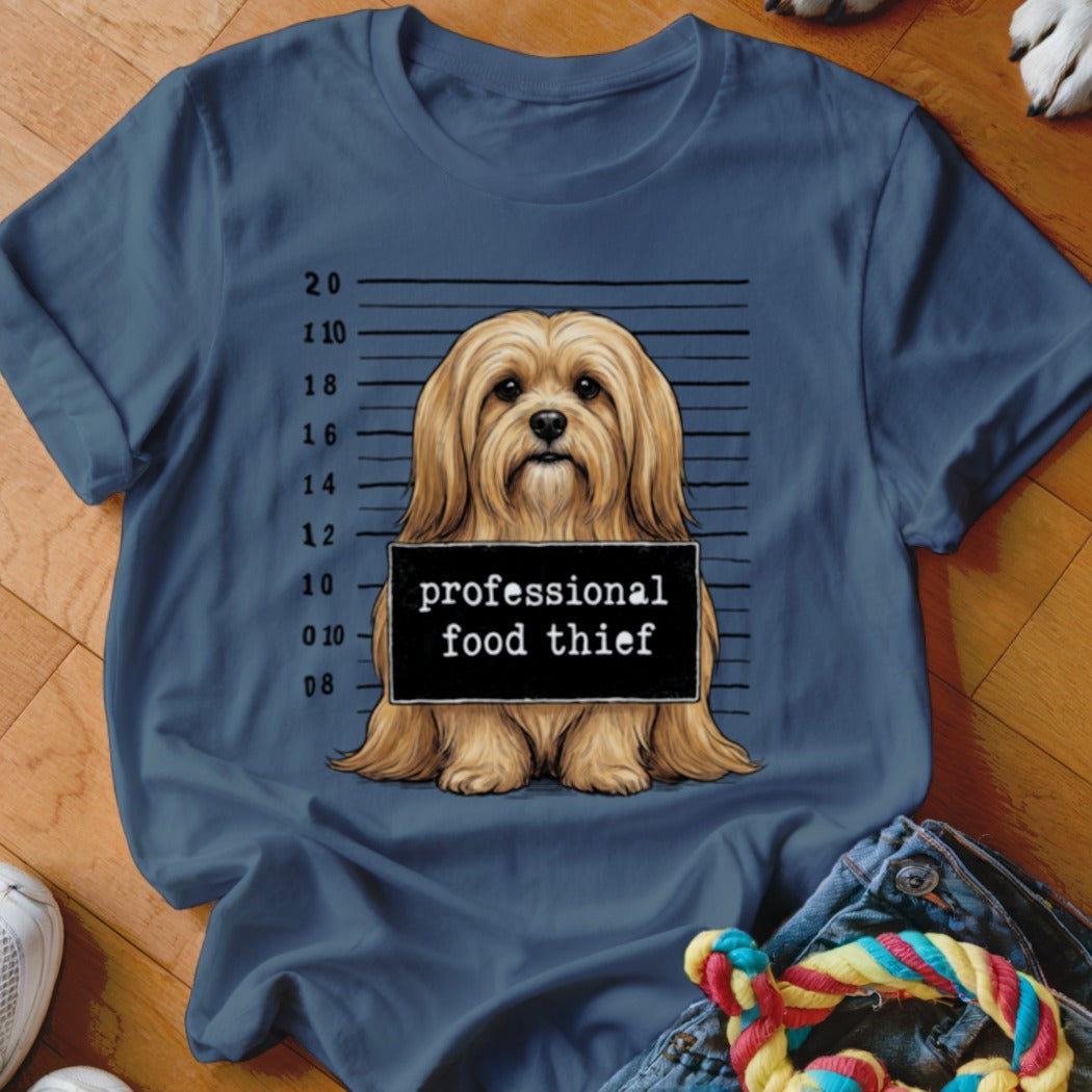 Dog mugshot with sign saying "professional food thief" on blue t-shirt.