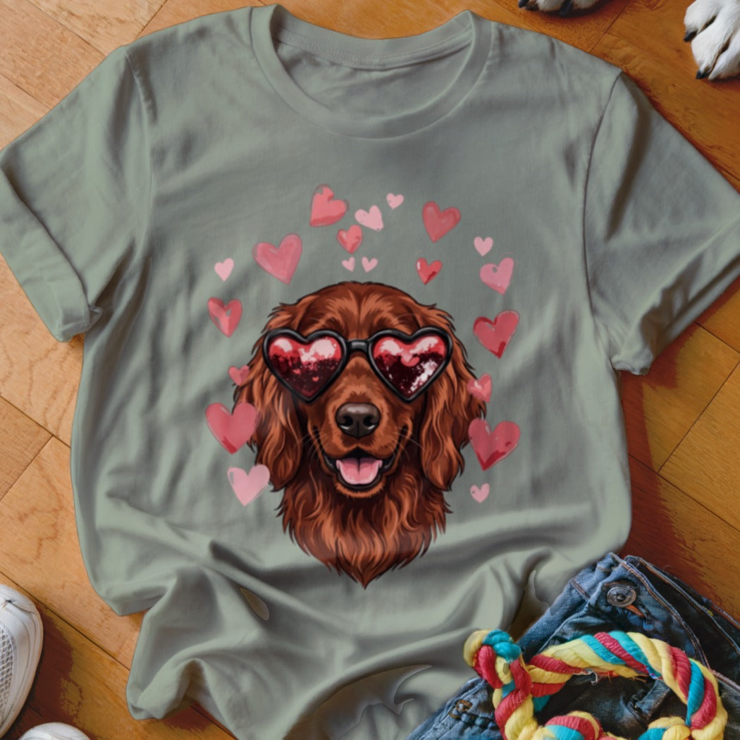 A sage green t-shirt features a graphic of a brown dog wearing heart-shaped sunglasses, surrounded by pink hearts.
