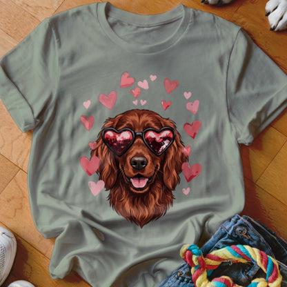 A sage green t-shirt features a graphic of a brown dog wearing heart-shaped sunglasses, surrounded by pink hearts.