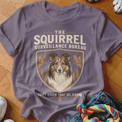 A dusty purple t-shirt displays text and a crest featuring a Shetland Sheepdog and squirrels.