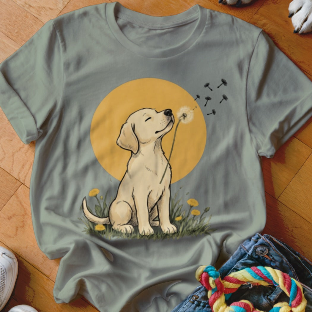 Sage green t-shirt featuring an illustration of a yellow Labrador puppy blowing a dandelion against a yellow circle background.