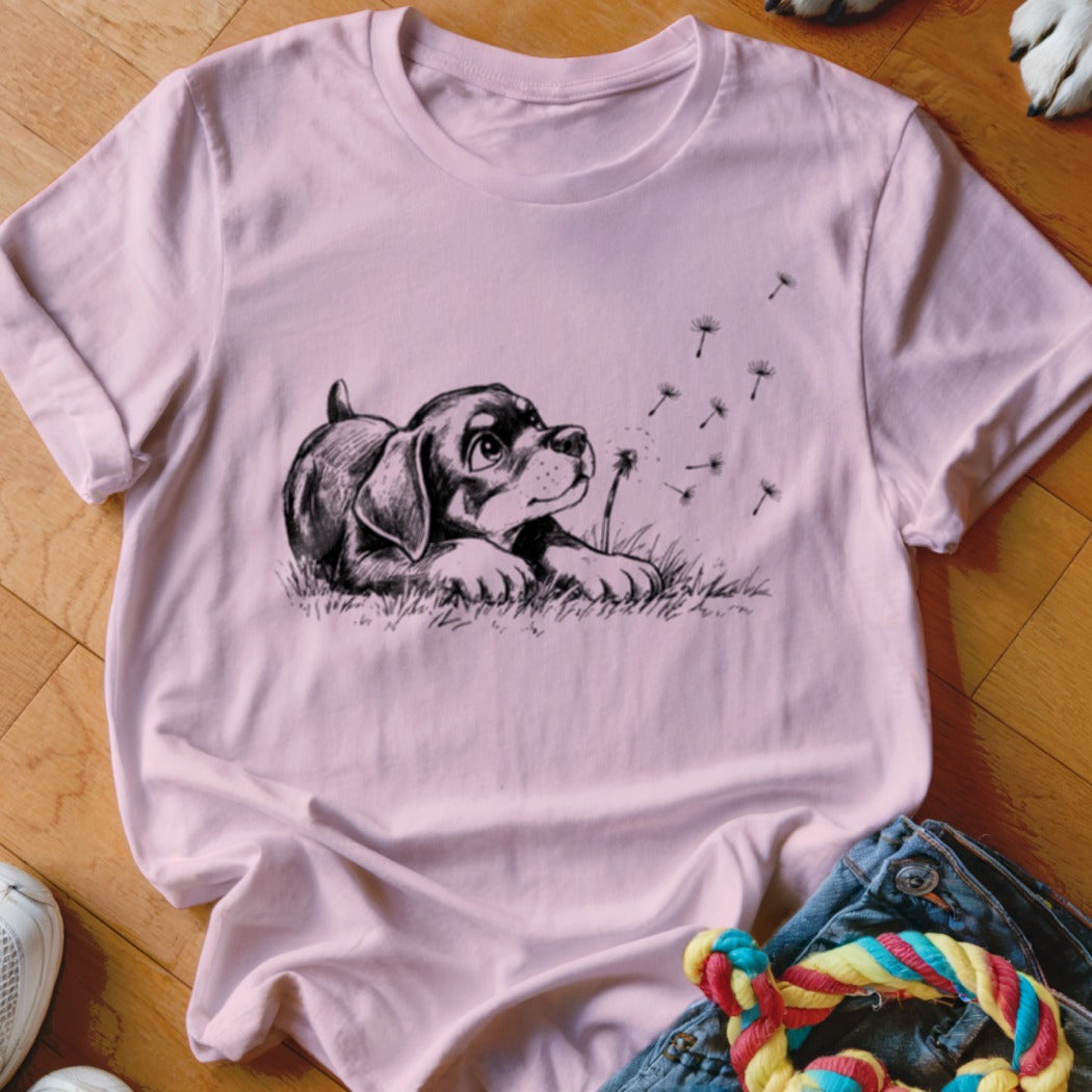 Light pink short-sleeved t-shirt featuring a black graphic of a puppy blowing dandelion seeds.